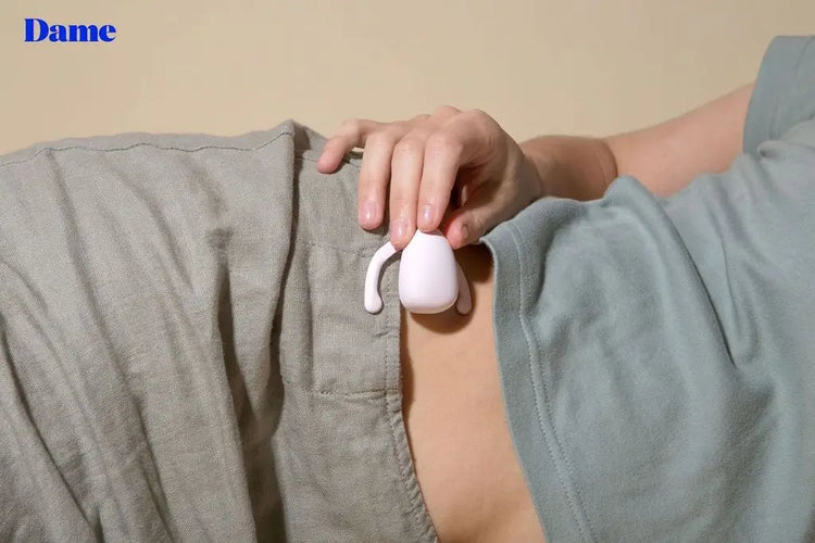 A woman lays on her side, holding Eva, the hands-free vibrator next to her stomach