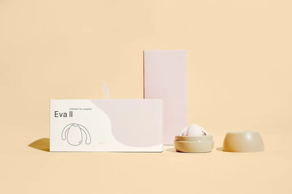 The Eva Two Hands-Free Vibrator is shown sitting inside of its case, next to its packaging box