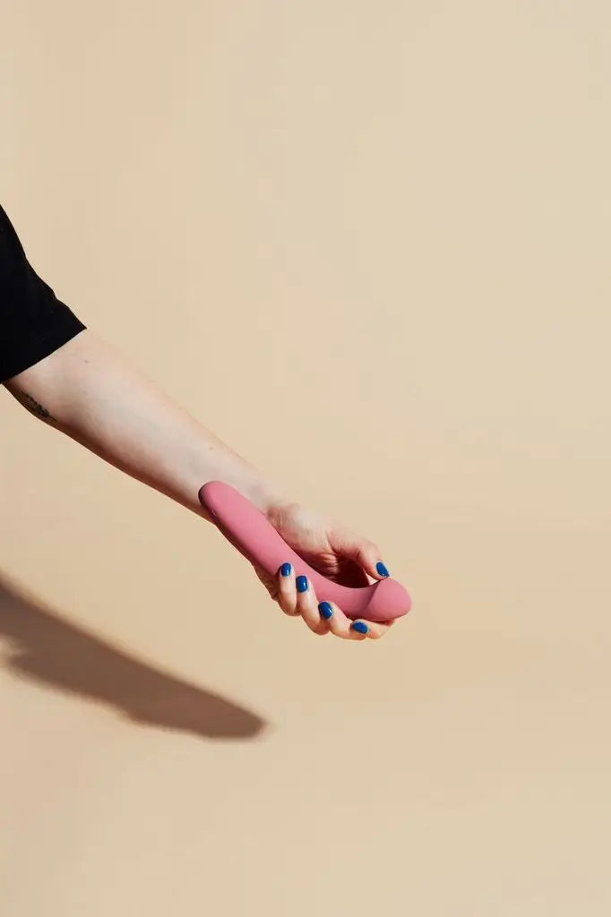 A person with blue nail polish holds a pink Arc, g-spot vibrator in their hand